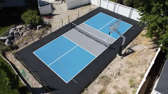 Blue and gray backyard net court with a black perimeter and basketball hoop.