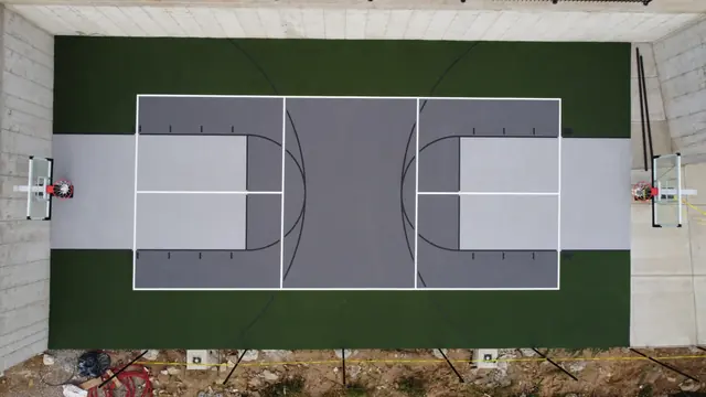 Overhead view of a gray basketball court with dark green borders and two hoops.