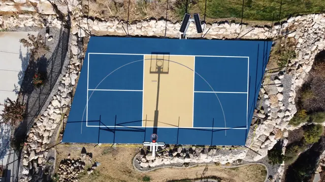 Blue and tan basketball court with black fencing and stone landscaping.