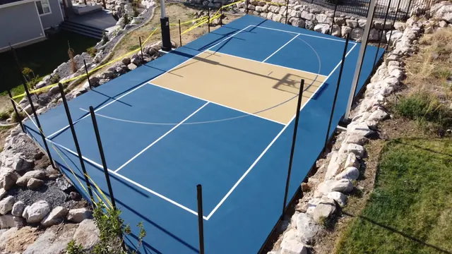 Blue and tan basketball court with black fencing and stone landscaping.