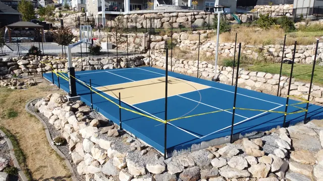 Blue and tan basketball court with black fencing and stone landscaping.