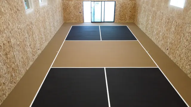Indoor net court with black playing areas, a tan center and white court lines.