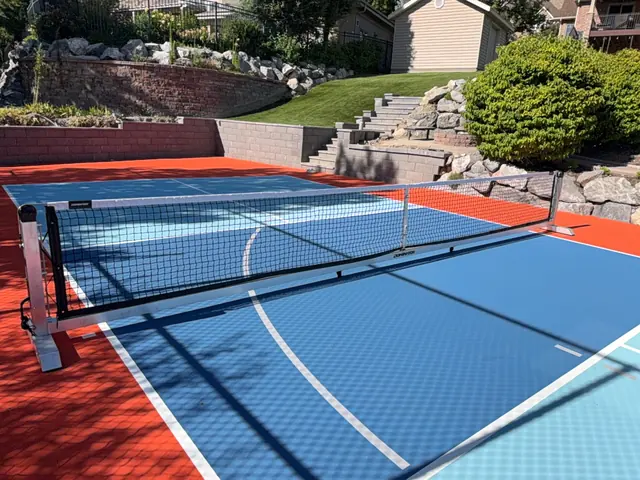 Backyard court with a bright orange border, blue playing areas, a net and basketball hoop.