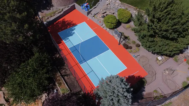 Backyard court with a bright orange border, blue playing areas, a net and basketball hoop.