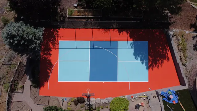 Backyard court with a bright orange border, blue playing areas, a net and basketball hoop.
