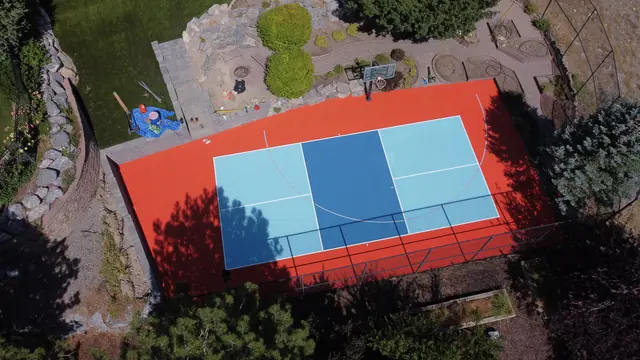 Backyard court with a bright orange border, blue playing areas, a net and basketball hoop.