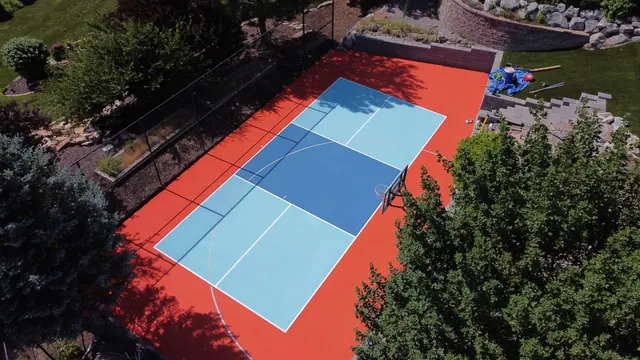 Backyard court with a bright orange border, blue playing areas, a net and basketball hoop.