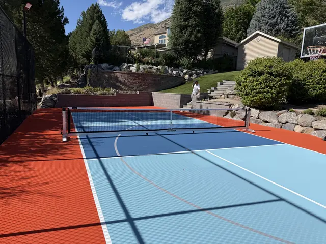 Backyard court with a bright orange border, blue playing areas, a net and basketball hoop.