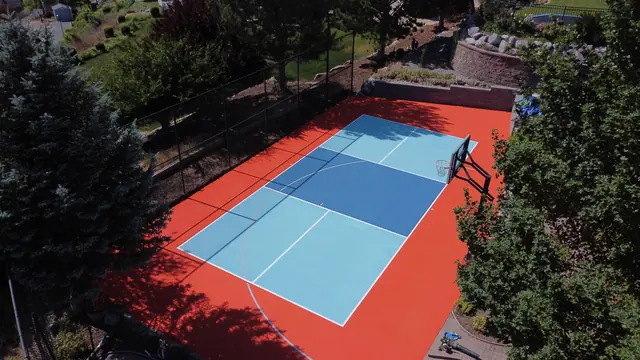 Backyard court with a bright orange border, blue playing areas, a net and basketball hoop.