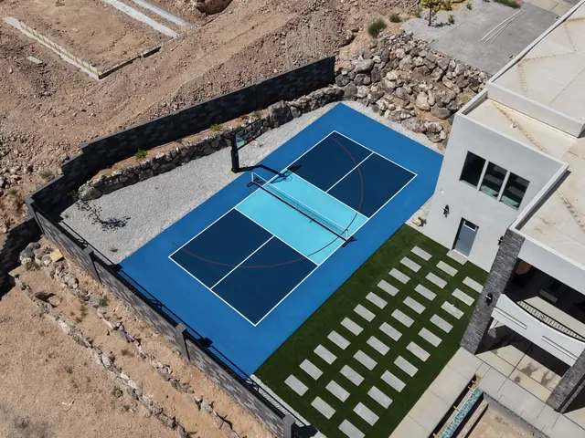 Blue backyard court with a light blue center, basketball hoop and net beside stone landscaping.