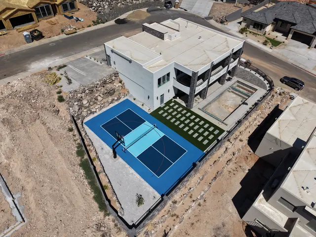 Blue backyard court with a light blue center, basketball hoop and net beside stone landscaping.
