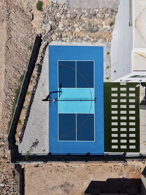 Blue backyard court with a light blue center, basketball hoop and net beside stone landscaping.