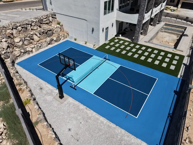 Blue backyard court with a light blue center, basketball hoop and net beside stone landscaping.