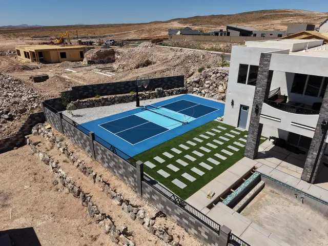 Blue backyard court with a light blue center, basketball hoop and net beside stone landscaping.