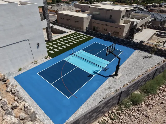 Blue backyard court with a light blue center, basketball hoop and net beside stone landscaping.