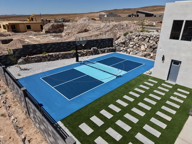 Blue backyard court with a light blue center, basketball hoop and net beside stone landscaping.