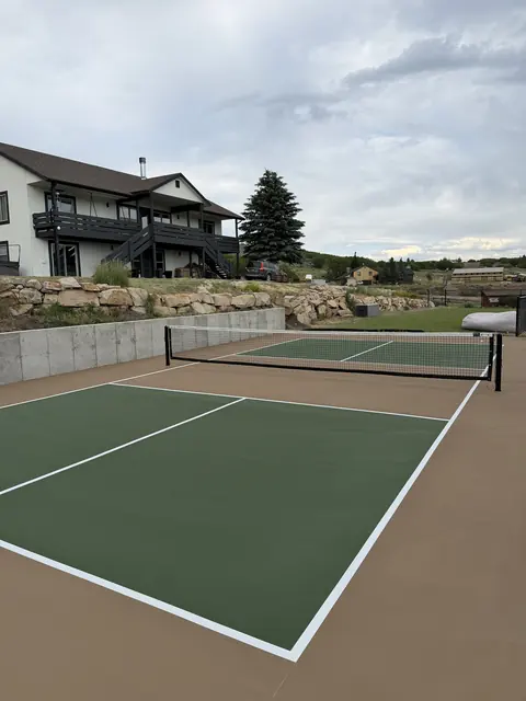 Green pickleball court with tan borders, a net and a concrete retaining wall.
