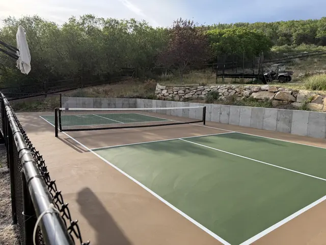 Green pickleball court with tan borders, a net and a concrete retaining wall.