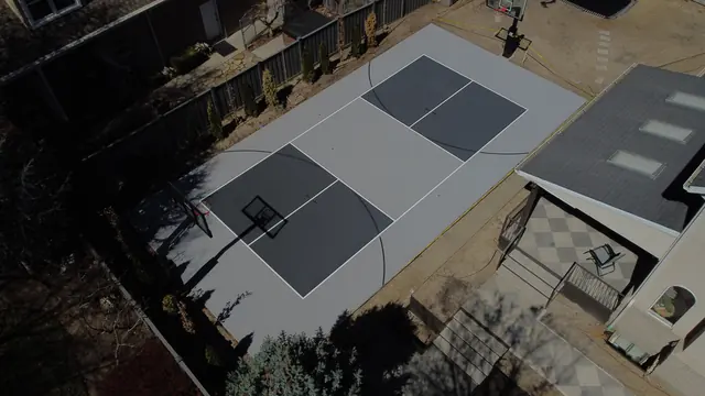Gray backyard basketball court with dark gray playing areas and two hoops.