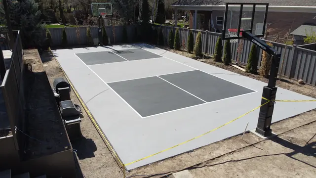 Gray backyard basketball court with dark gray playing areas and two hoops.