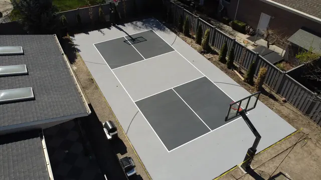 Gray backyard basketball court with dark gray playing areas and two hoops.