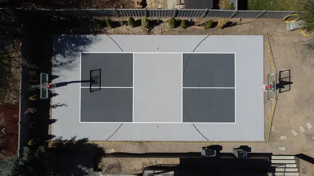 Gray backyard basketball court with dark gray playing areas and two hoops.