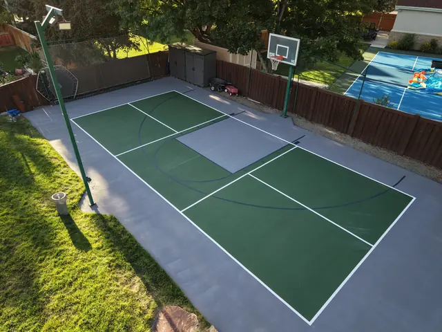 Green and gray backyard court with basketball and net-game markings beside a lawn.