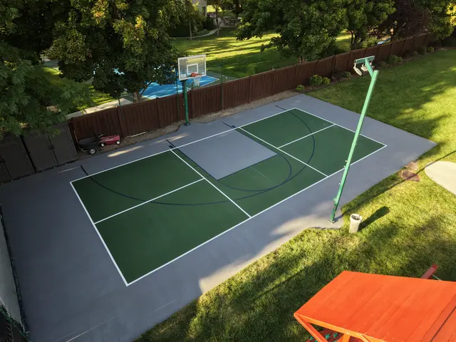Green and gray backyard court with basketball and net-game markings beside a lawn.