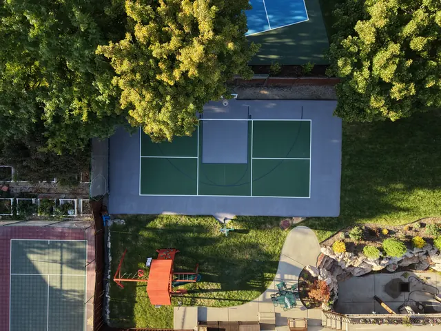 Green and gray backyard court with basketball and net-game markings beside a lawn.
