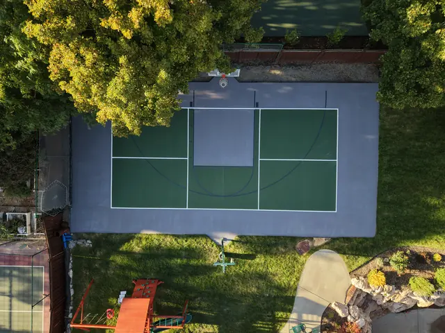Green and gray backyard court with basketball and net-game markings beside a lawn.