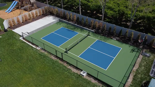 Blue pickleball playing areas with green borders, a center net and black perimeter fencing.