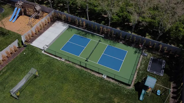 Blue pickleball playing areas with green borders, a center net and black perimeter fencing.