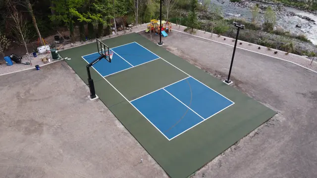Blue and green backyard basketball court with two hoops and tall light poles.