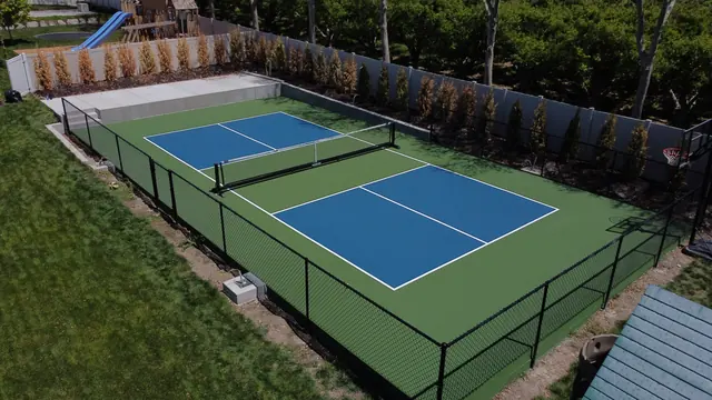 Blue pickleball playing areas with green borders, a center net and black perimeter fencing.
