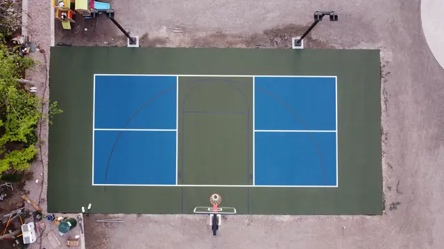 Blue and green backyard basketball court with two hoops and tall light poles.