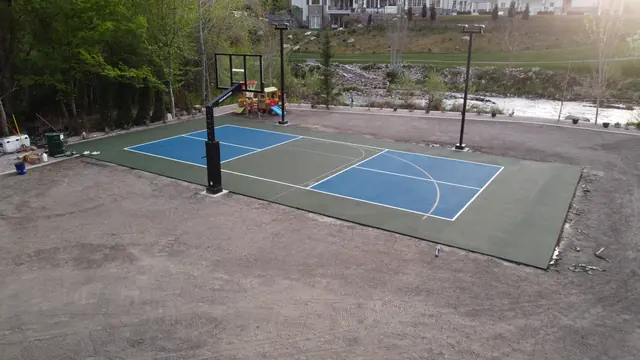 Blue and green backyard basketball court with two hoops and tall light poles.