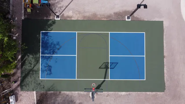 Blue and green backyard basketball court with two hoops and tall light poles.