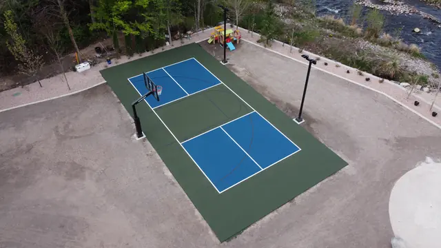 Blue and green backyard basketball court with two hoops and tall light poles.