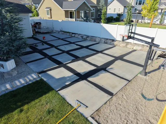 Existing backyard court surface with a grid of dark repair areas before resurfacing.