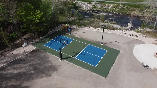 Blue and green backyard basketball court with two hoops and tall light poles.