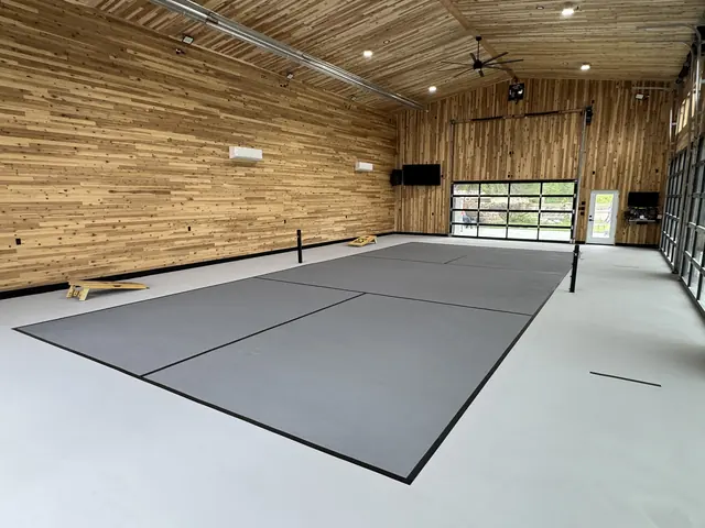Indoor gray net court with black lines in a wood-paneled recreation building.