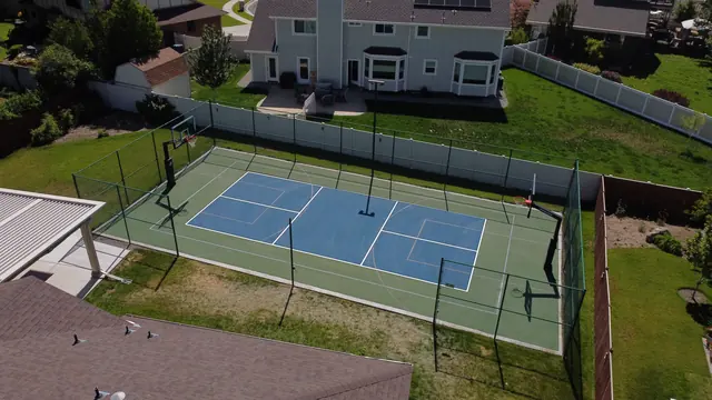 Blue and green backyard court with black fencing, a center net and basketball hoops.