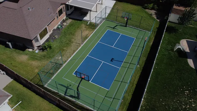 Blue and green backyard court with black fencing, a center net and basketball hoops.