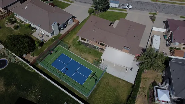 Blue and green backyard court with black fencing, a center net and basketball hoops.