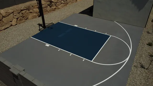 Compact gray basketball half court with a dark blue key beside a home.