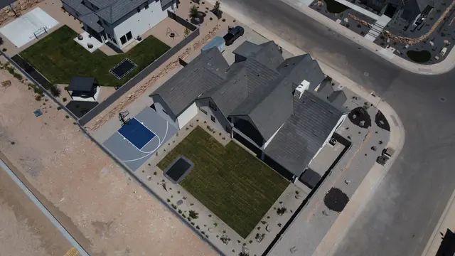 Compact gray basketball half court with a dark blue key beside a home.