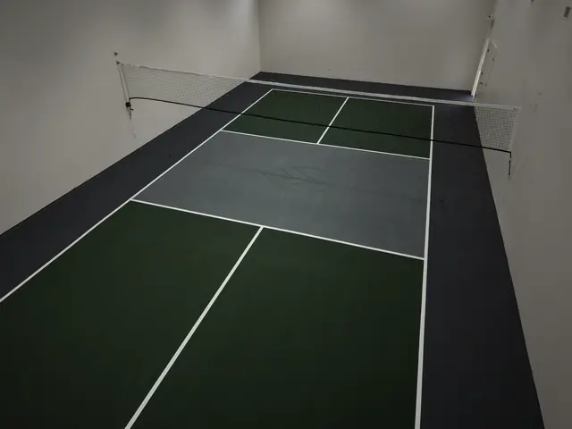 Indoor pickleball court with green playing areas, a gray center, black borders and a net.