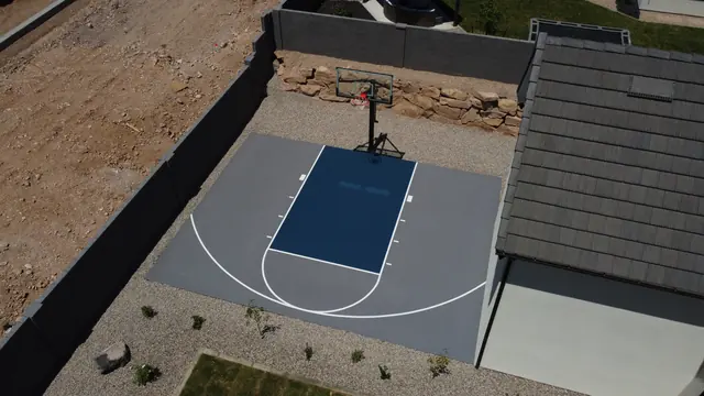 Compact gray basketball half court with a dark blue key beside a home.