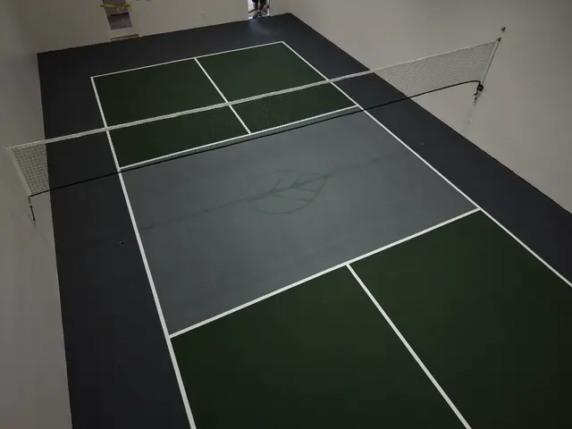 Indoor pickleball court with green playing areas, a gray center, black borders and a net.