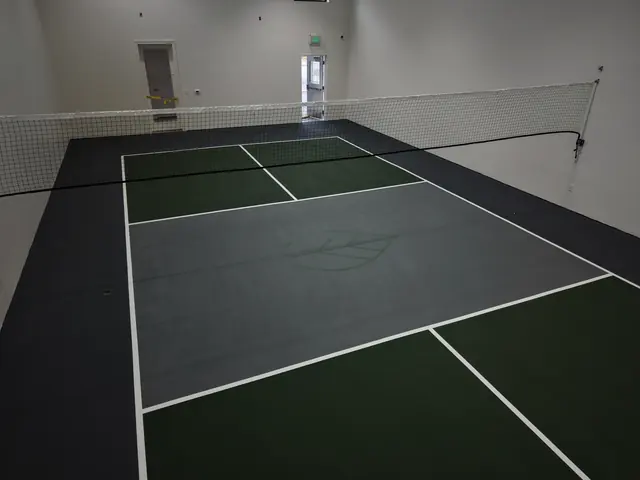 Indoor pickleball court with green playing areas, a gray center, black borders and a net.